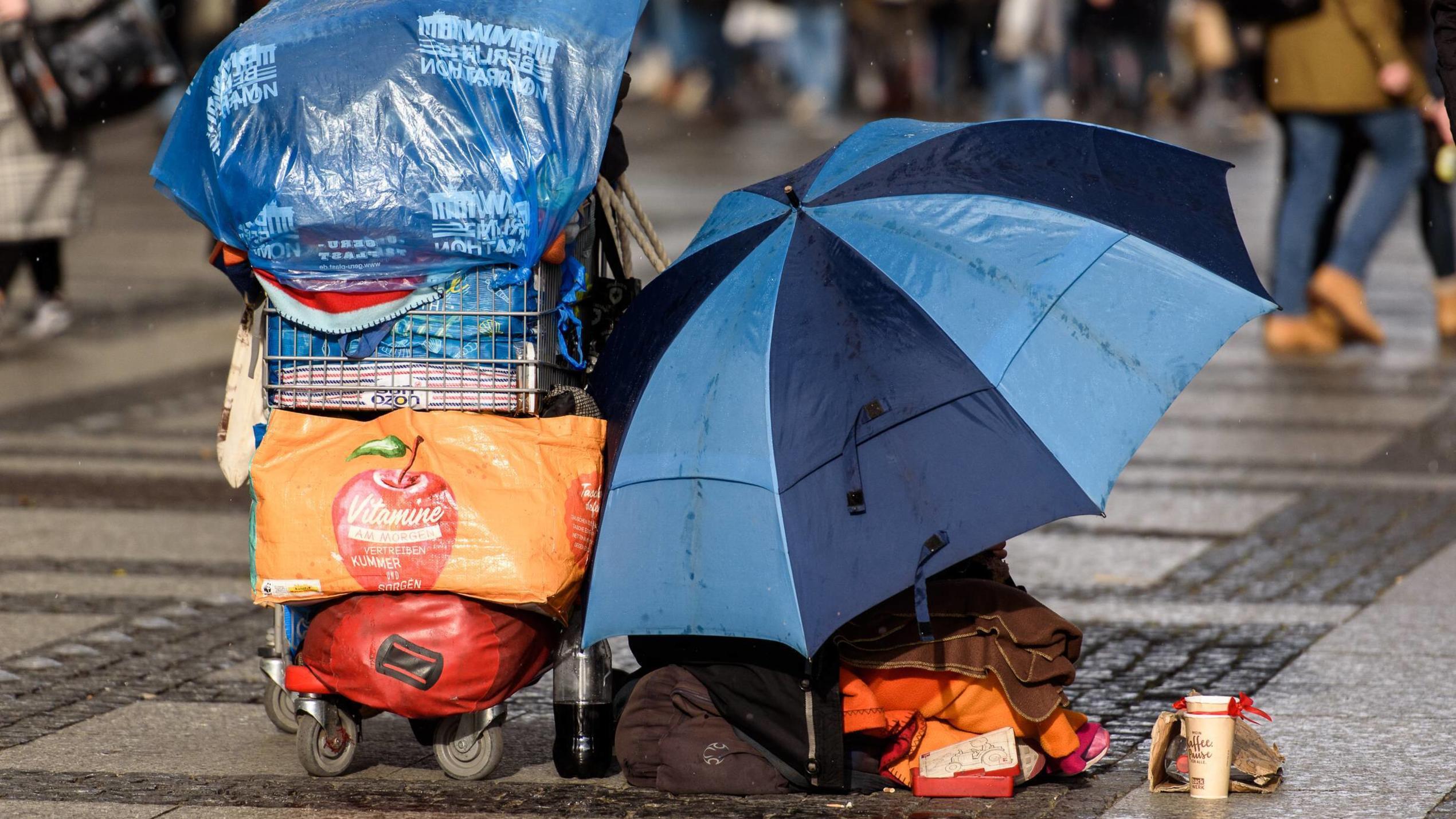 Müssen Menschen in Deutschland auf der Straße leben? Feature Bild Obdachlosigkeit Deutschland, Berlin - 09/03/2019: Im Bild ist ein Obdachloser Mensch mit Schirm und Einkaufswagen sitzend auf der Straße zu sehen. Berlin Berlin Deutschland *** Feature Picture Homelessness Germany Berlin 09 03 2019 The