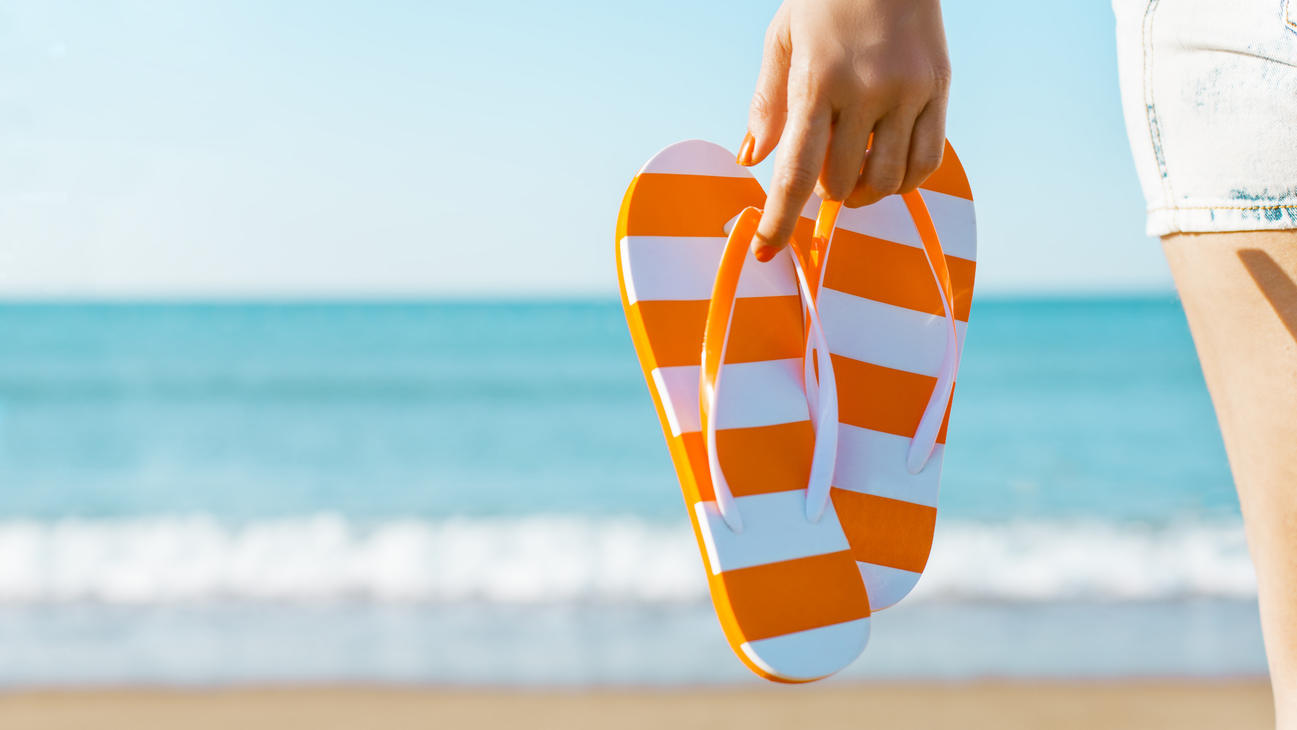 Fashion Lexikon: Flip-Flops Frau hält orangene Sandalen