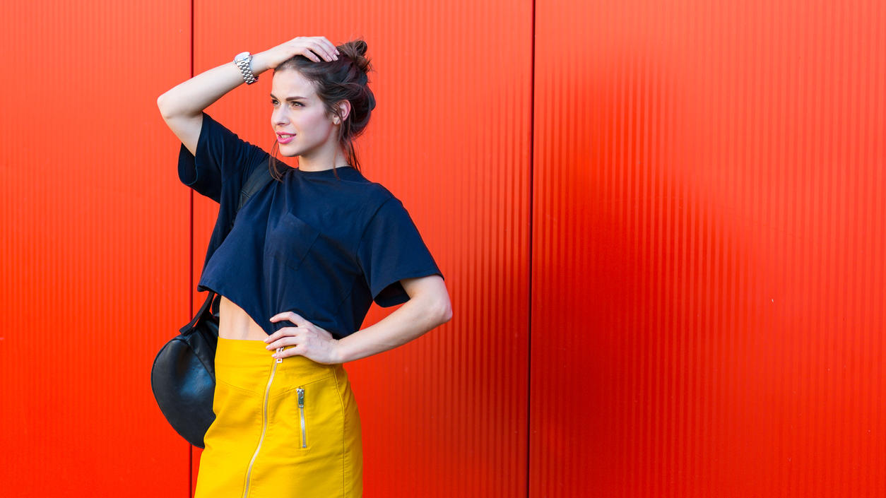 Fashion Lexikon: Colour Blocking Junge modebewusste Frau trägt ein dunkelblaues T-Shirt mit einem gelben Rock. Dieser Look nennt sich Colour Blocking.