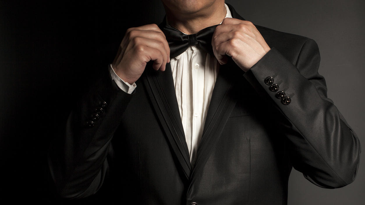 Fashion Lexikon: Black Tie / White Tie Ein Mann bindet sich eine schwarze Fliege um