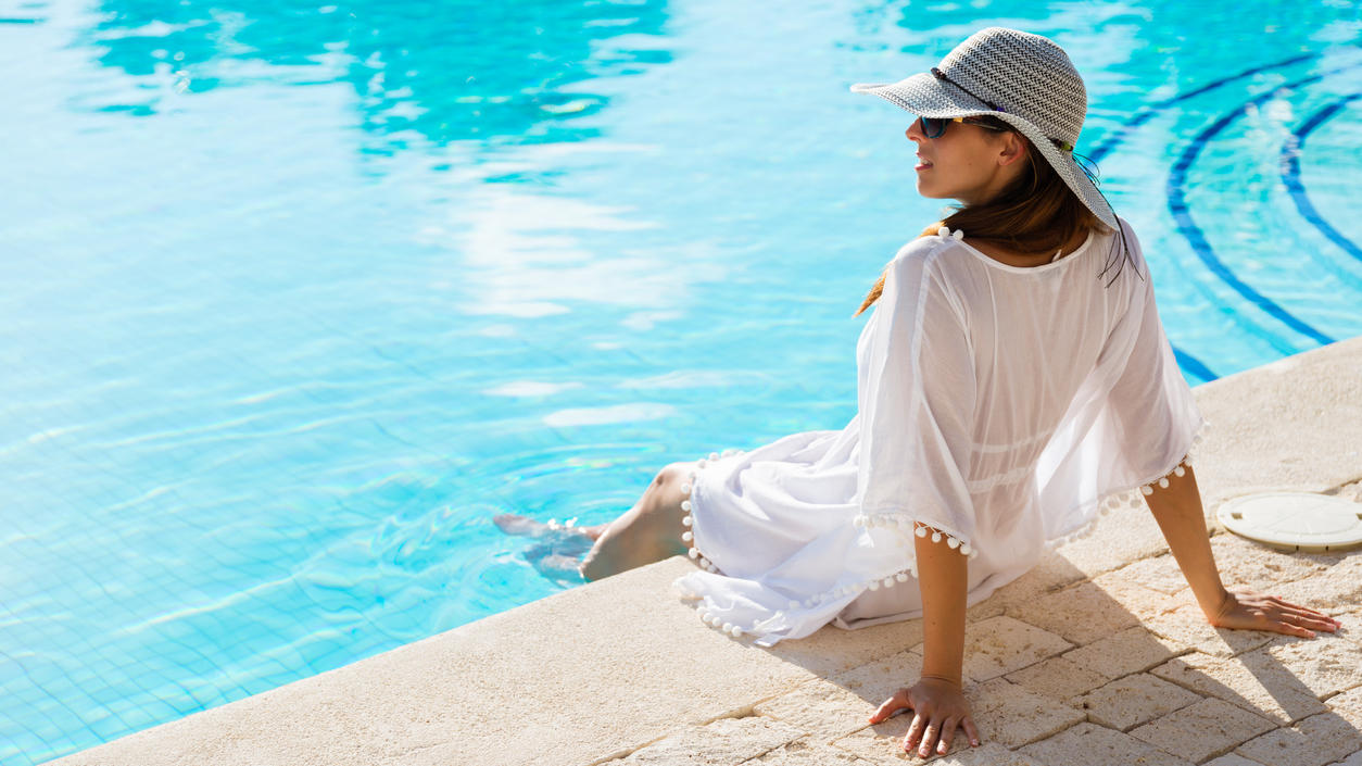 Fashion Lexikon: Kaftan Frau im weißen Kaftan mit Sonnenbrille und Sonnenhut