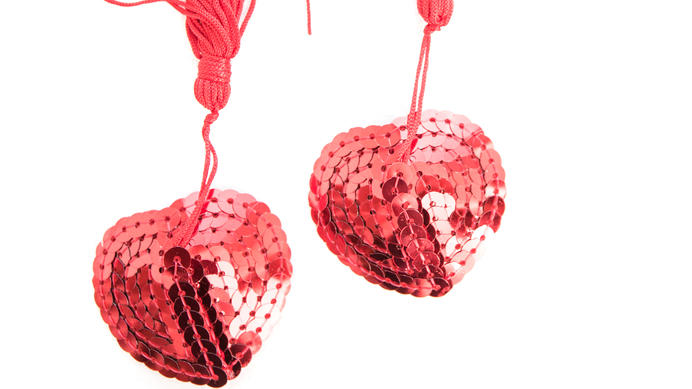 Fashion Lexikon: Pasties Zwei rote glitzernde Pasties zur Bedeckung der weiblichen Brustwarzen und des Intimbereiches.