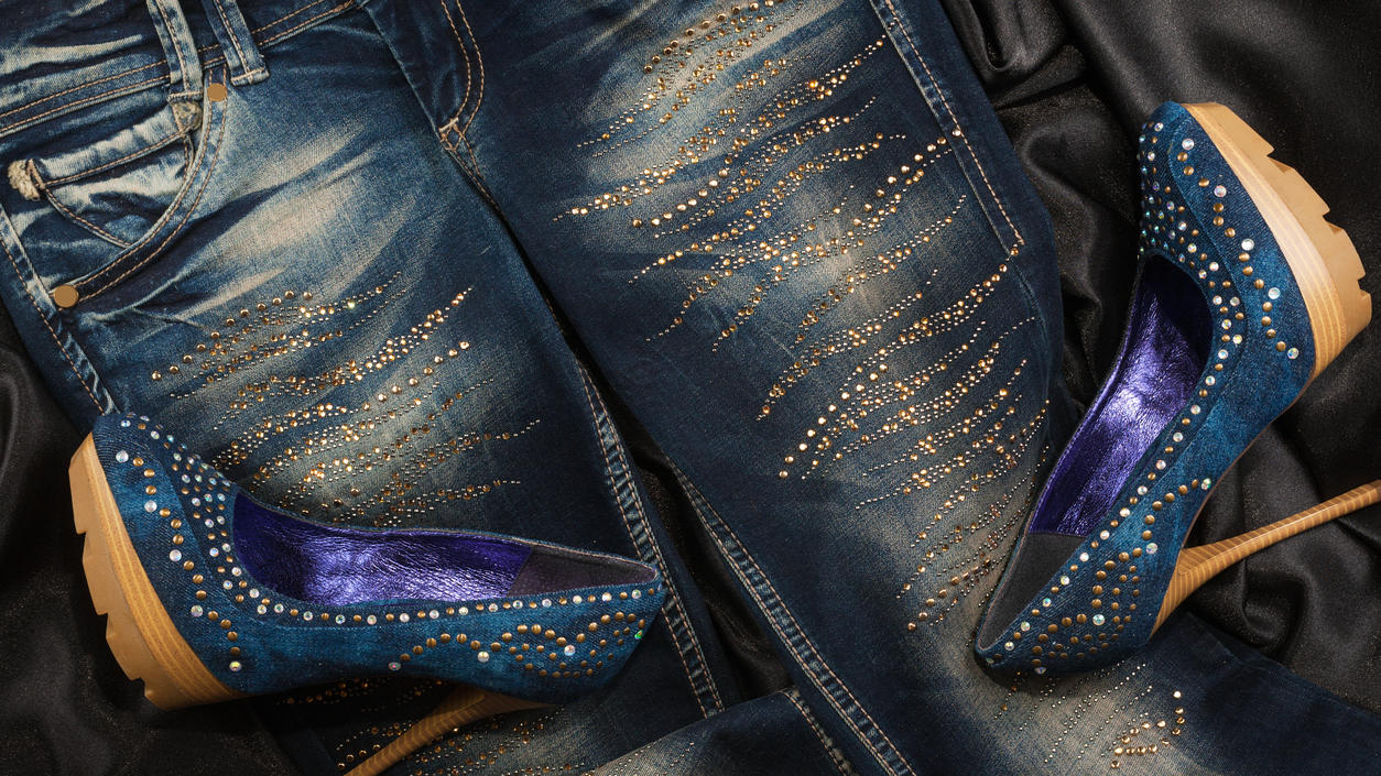 Fashion Lexikon: Strass Hier liegen zwei dunkelblaue High Heels auf einer mit Strass verzierten Jeans.