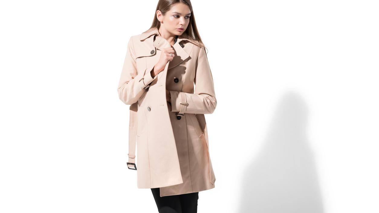 Fashion Lexikon: Trenchcoat Junge Frau in einem beigefarbenen Trenchcoat