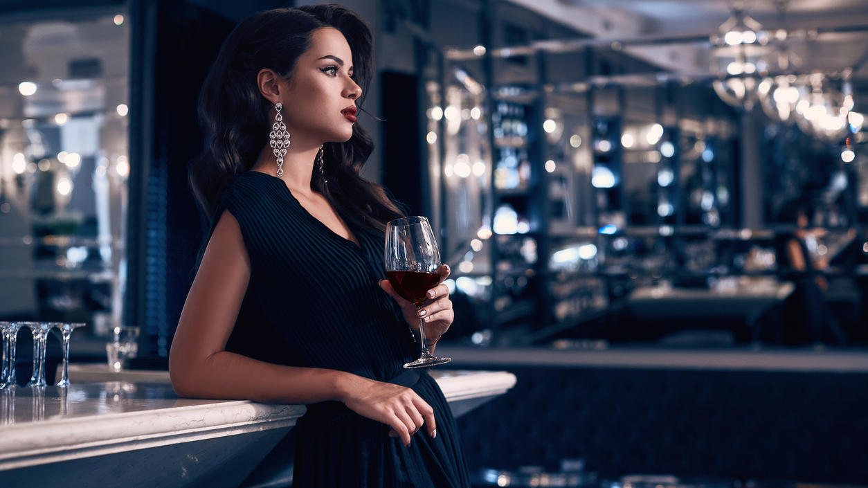 Fashion Lexikon: Elegant Stilvolle Frau in elegantem Kleid mit einem Glas Wein in der Hand