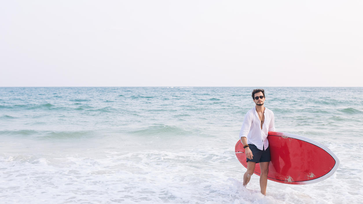 Fashion Lexikon: Bermudas Mann mit rotem Surfbrett in Bermudas