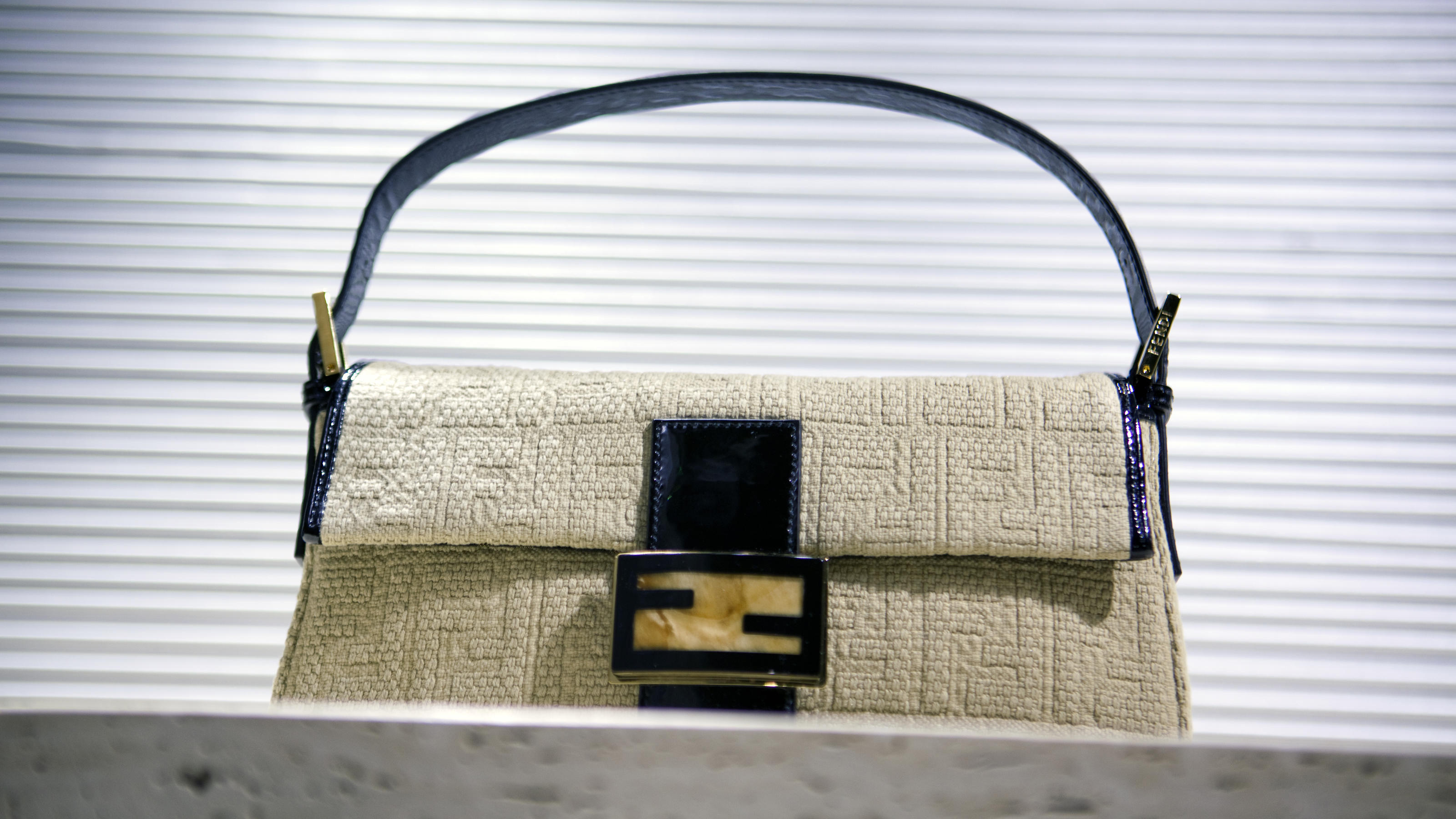 Fashion Lexikon: It-Bag Trendige It-Bag steht auf einer Fensterbank und hat einen dunkelblauen Taschenhenkel.