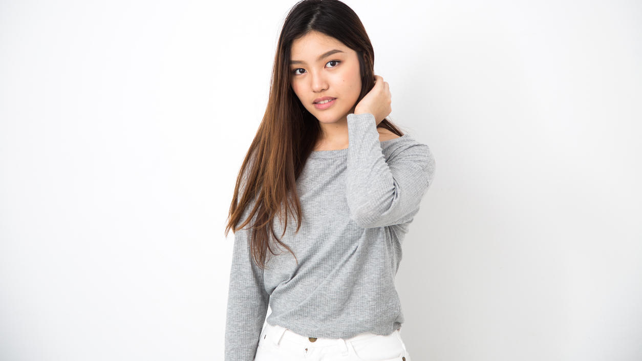 Fashion Lexikon: Langarmshirt Asiatische Frau steht vor einem weißen Hintergrund und trägt ein graues Langarmshirt.