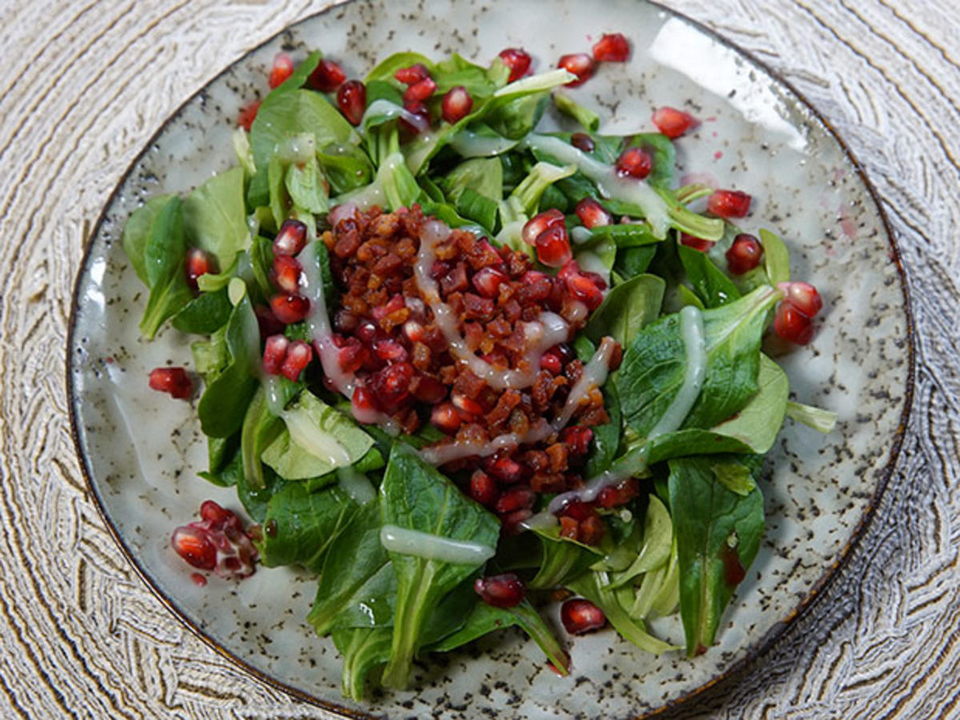 Feldsalat mit Granatapfelkernen und Speckwürfeln an Kartoffeldressing